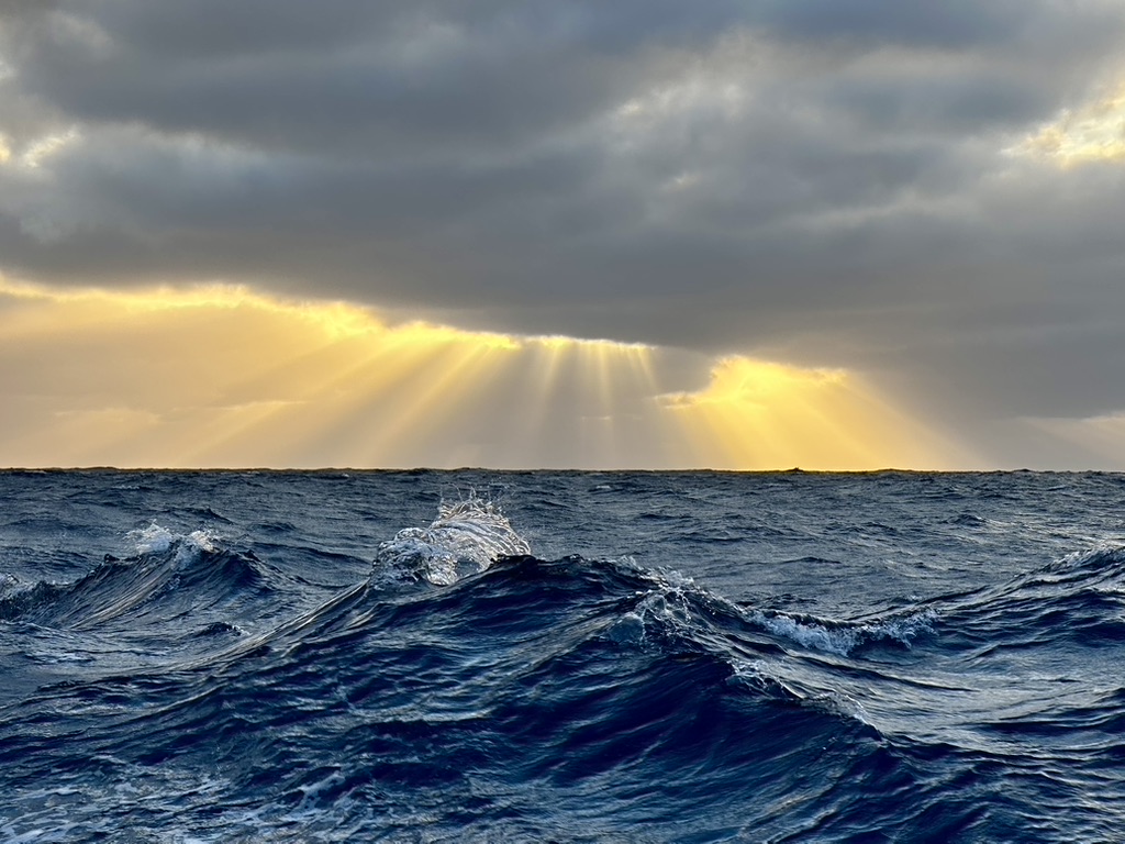 Sunlight breaking through clouds above rolling ocean waves